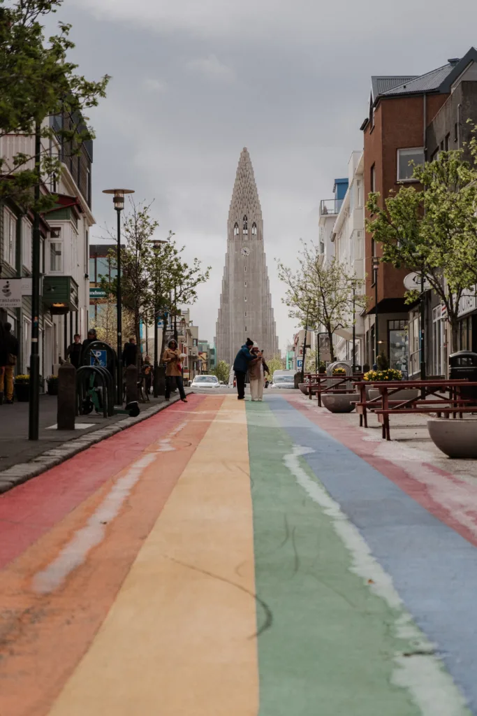 Dominantou celého snímku je šedá betonová věž kostela Hallgrímskirkja, která se tyčí přímo v ose ulice proti zamračené obloze.