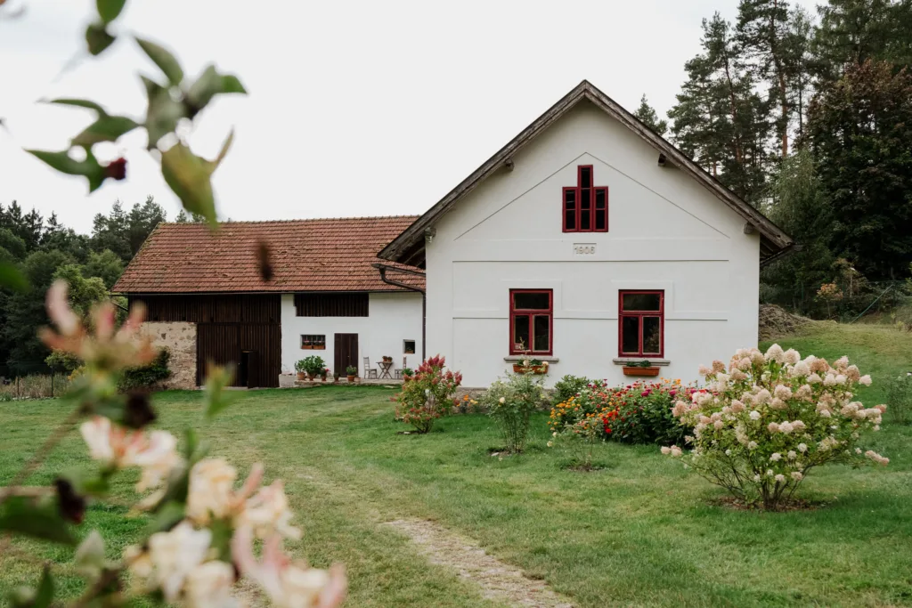 Pohled na historickou chalupu s červenými okny a rozkvetlou zahradou na svatebním místě Samota Křemen.