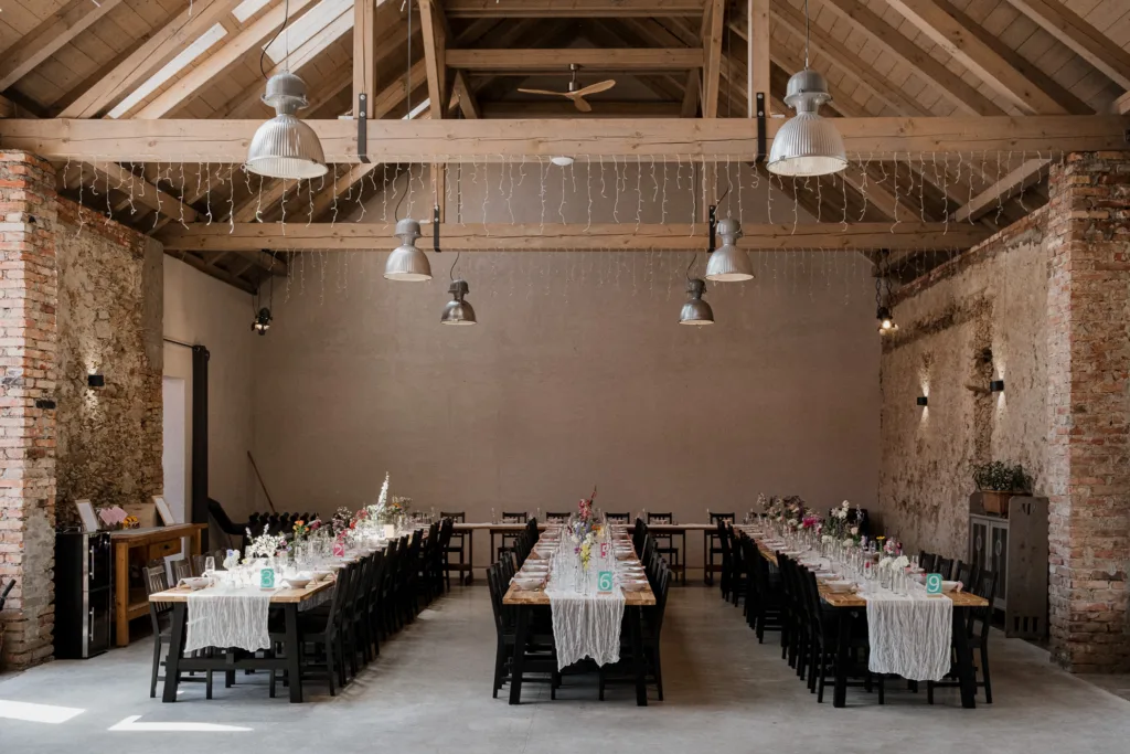 Interiér svatební stodoly na Statku Šemíkovice s kamennými zdmi, dřevěným krovem a prostřenou svatební tabulí.